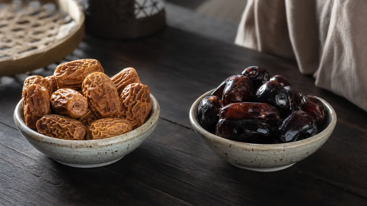 Dua mangkuk kurma berdampingan, satu berisi kurma kering dan satu berisi kurma basah berkilap